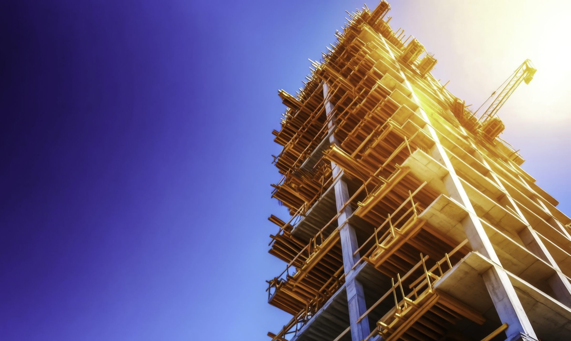 high rise construction building under bright blue sky with sunlight reflections on scaffolding